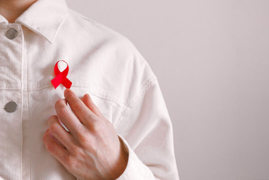Mann mit roter Schleife am Hemd zum Welt-AIDS-Tag